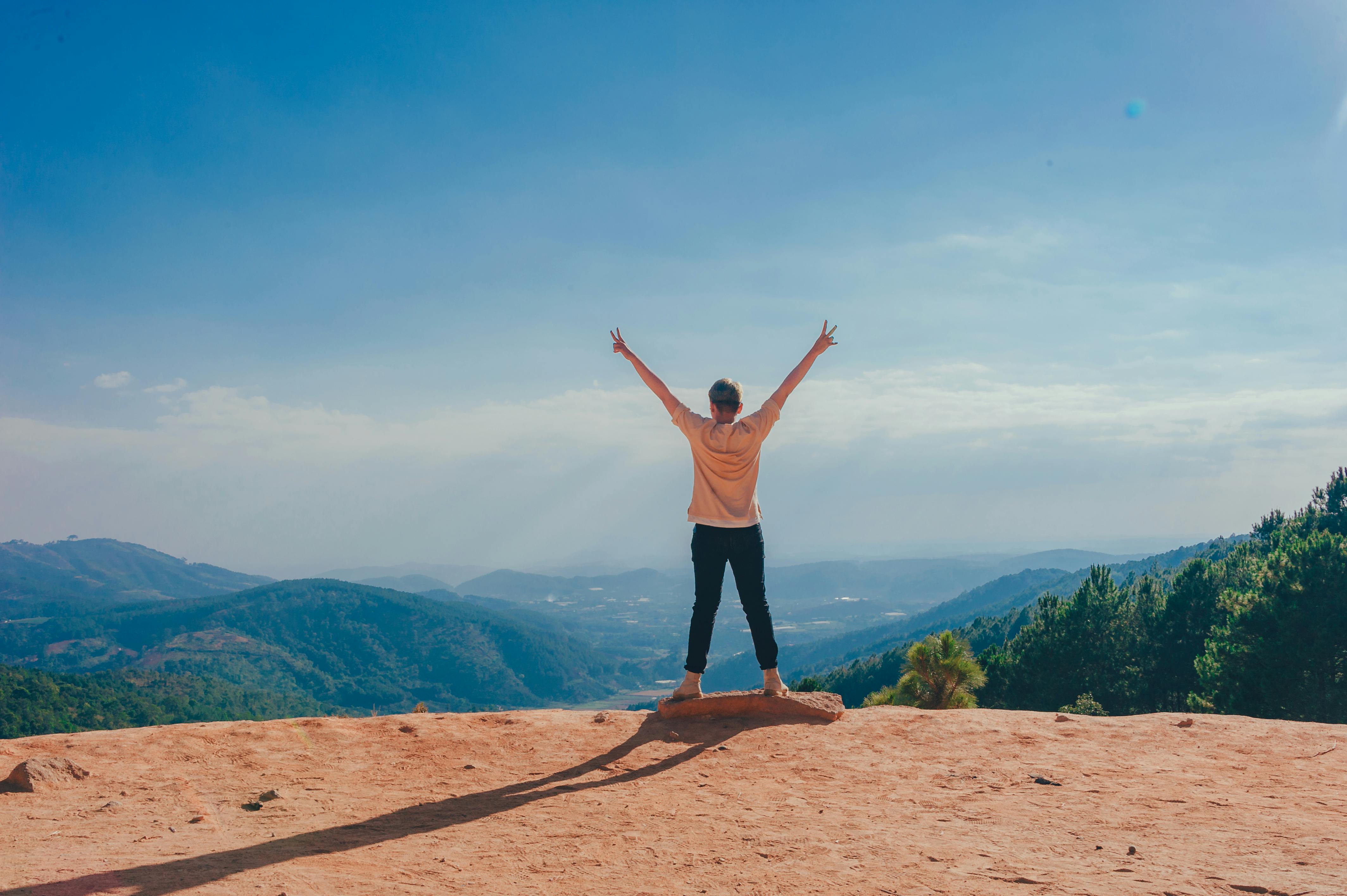 Foto met vrouw die juichend op de rand van een klif staat, door Min An van Pexels: https://www.pexels.com/photo/woman-standing-on-cliff-1134190/